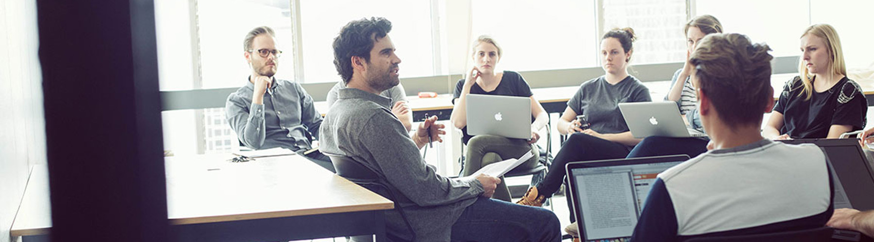 people sitting down with laptops watching a man teach a tutorial